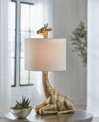 Gold table lamp with sculpted giraffe base and cream fabric drum shade.