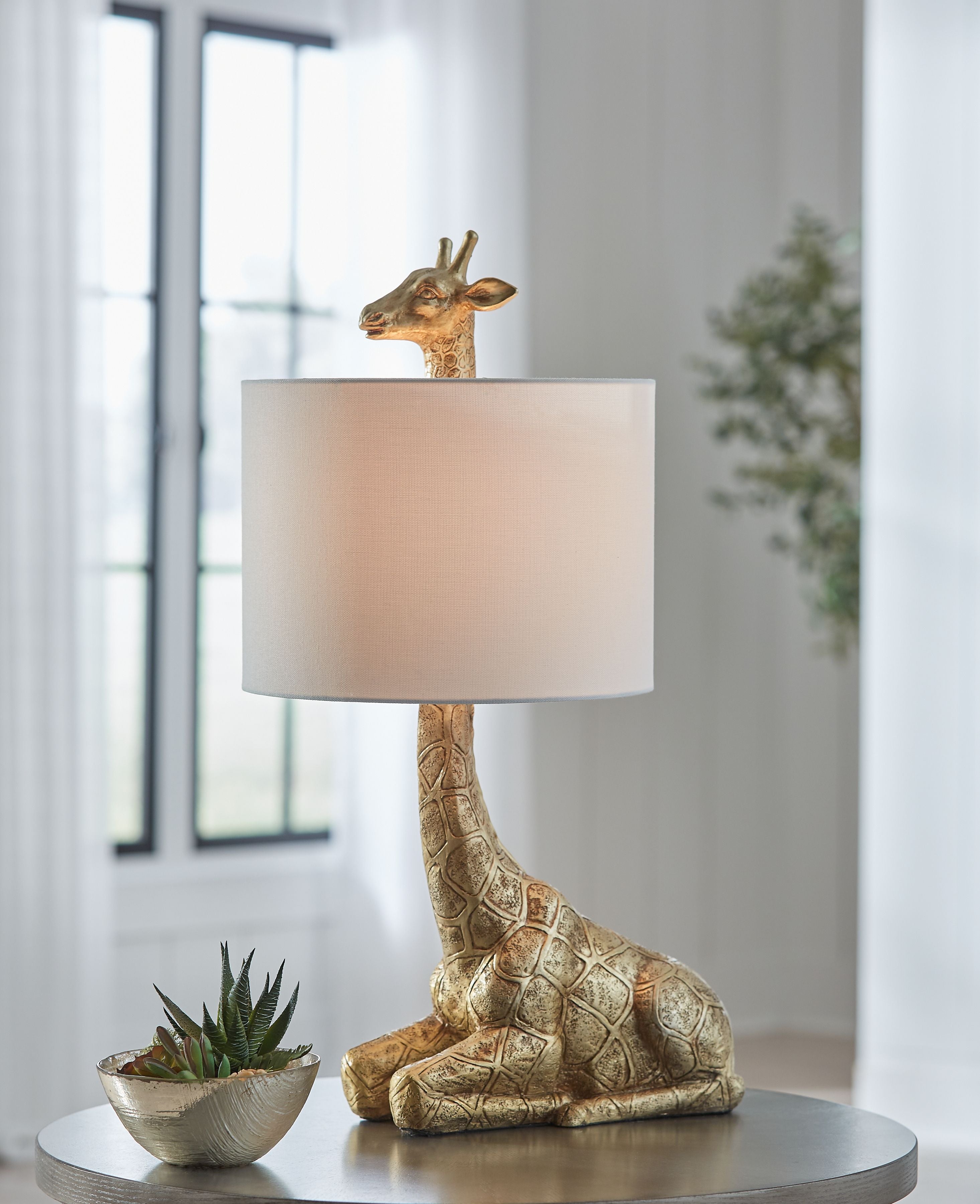 Gold table lamp with sculpted giraffe base and cream fabric drum shade.