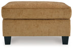 Light brown ottoman with upholstered round top, visible seams, dark block legs
