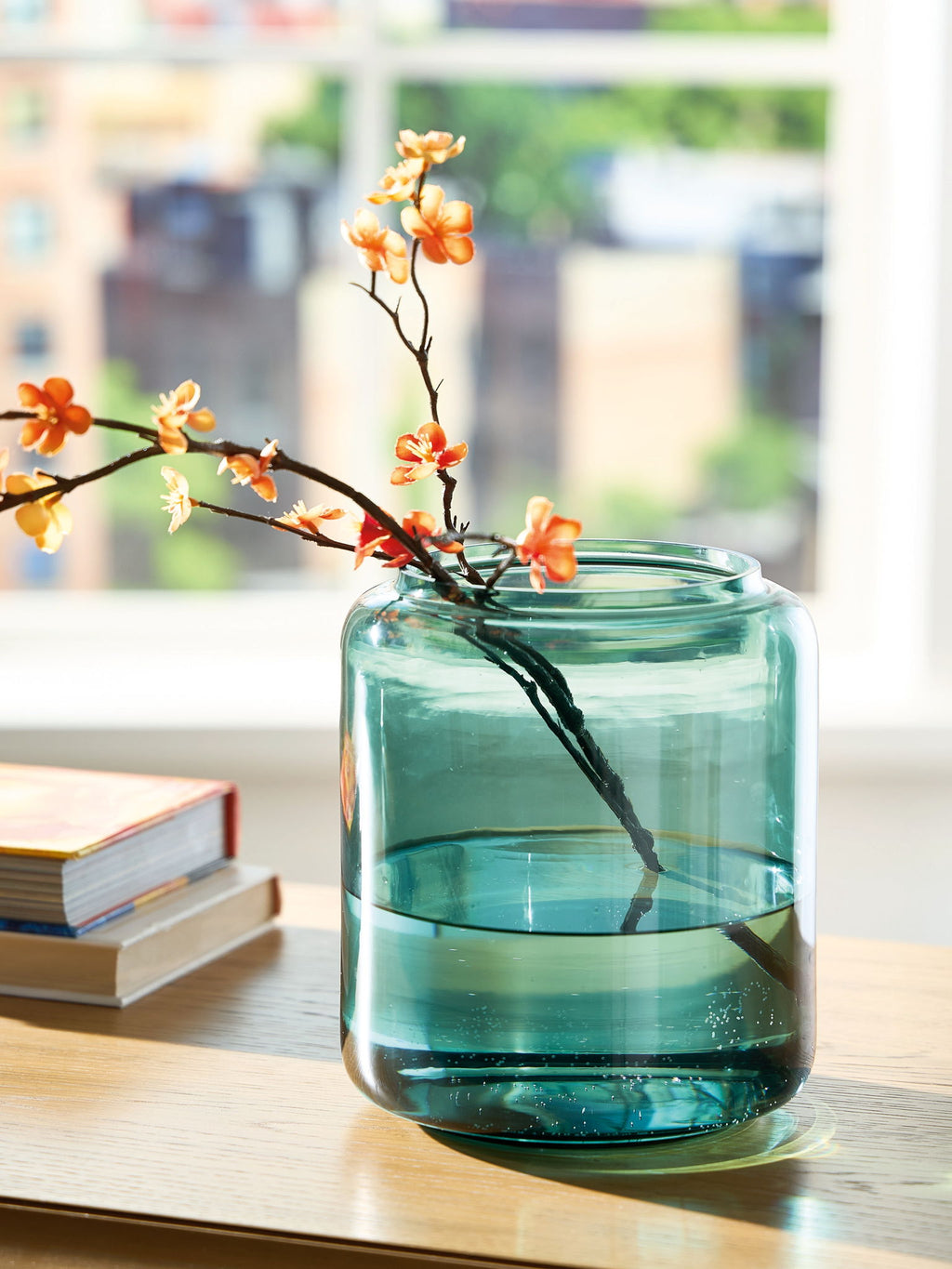 Teal glass vase with curved sides and small orange blossoms