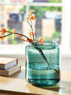 Teal glass vase with curved sides and small orange blossoms