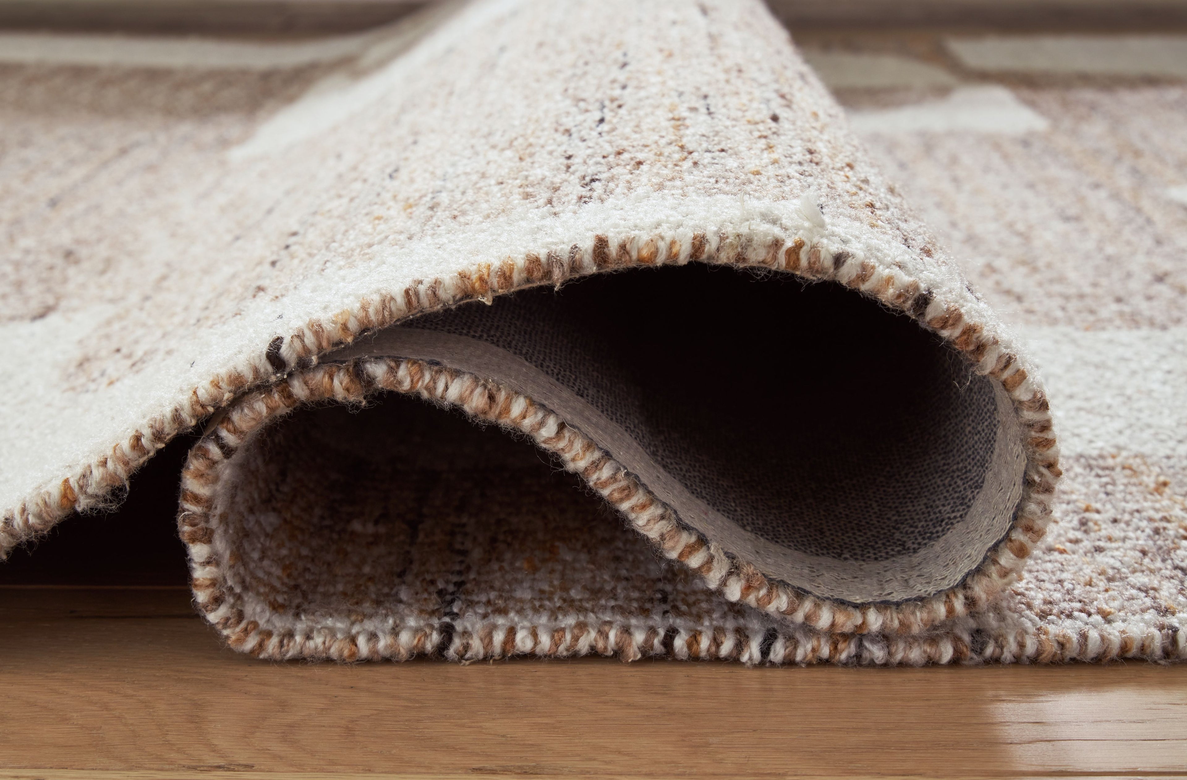 Beige rug with rounded bound border and short textured pile, underside visible