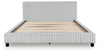 Upholstered bed with light ribbed frame and headboard, uncovered beige mattress base