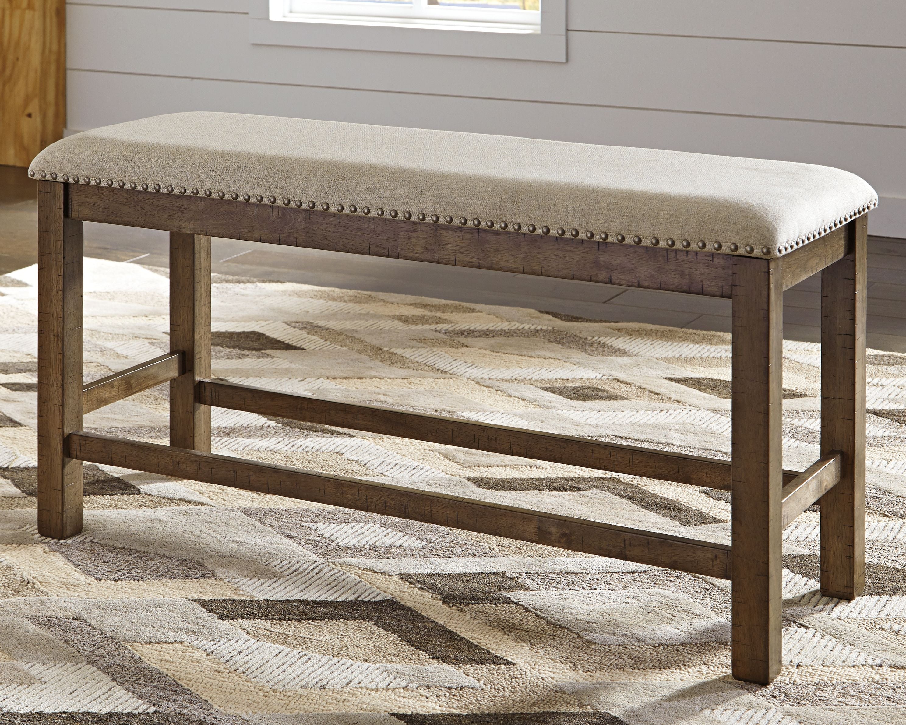 Beige upholstered bench with nailhead trim, open base frame, and dark wood legs