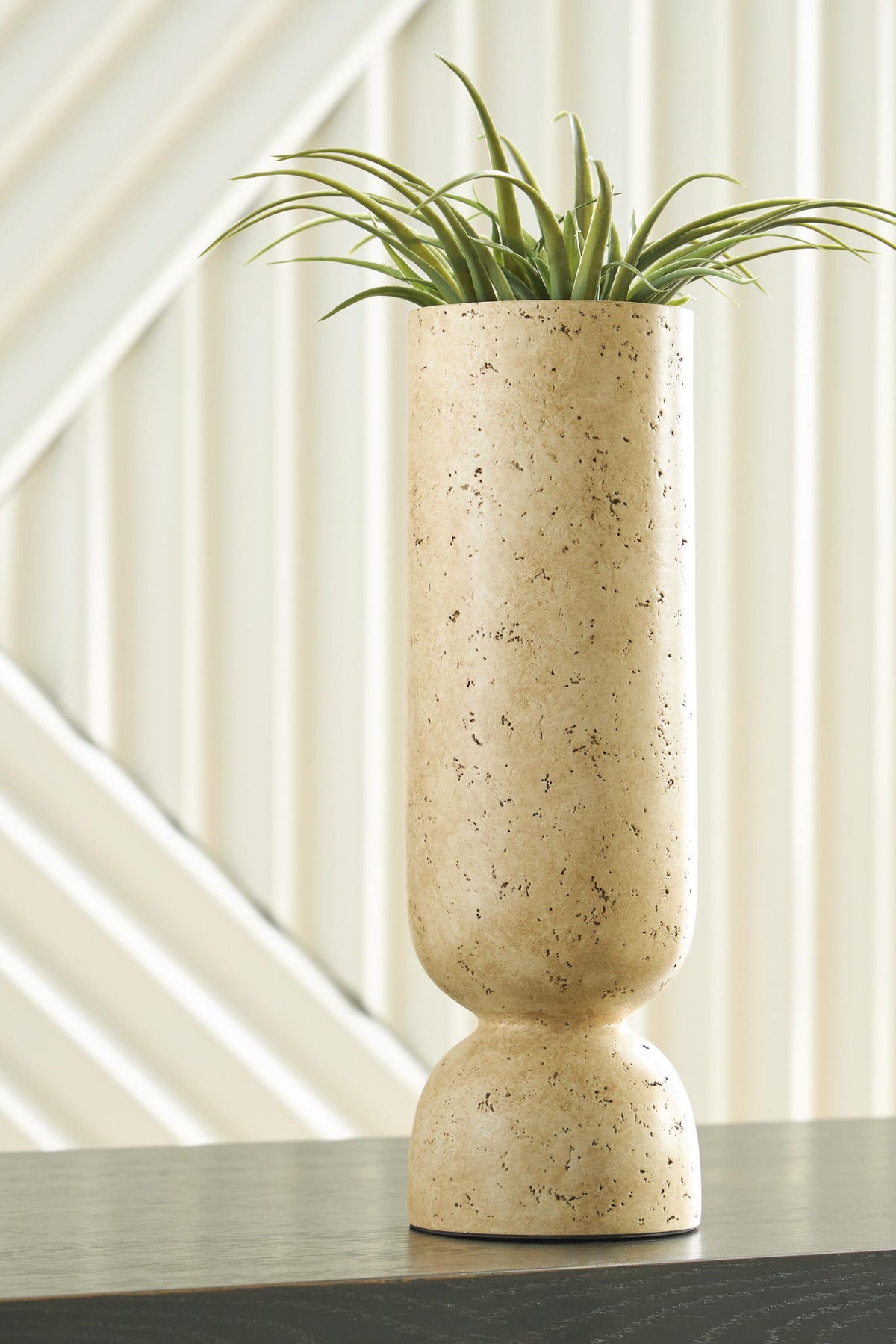 Beige speckled vase on tabletop holding green grass stems