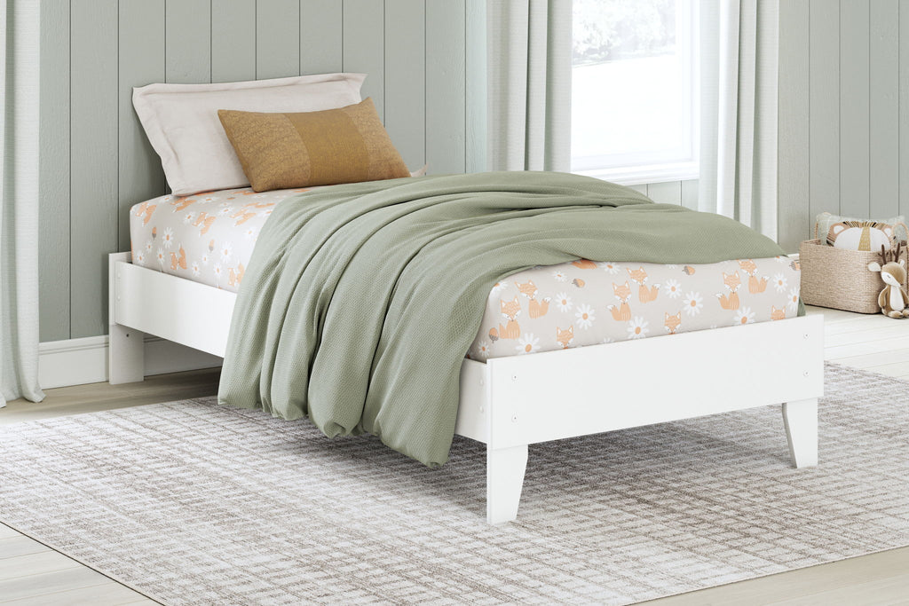 White platform bed with upholstered headboard, decorative pillows, and draped quilt