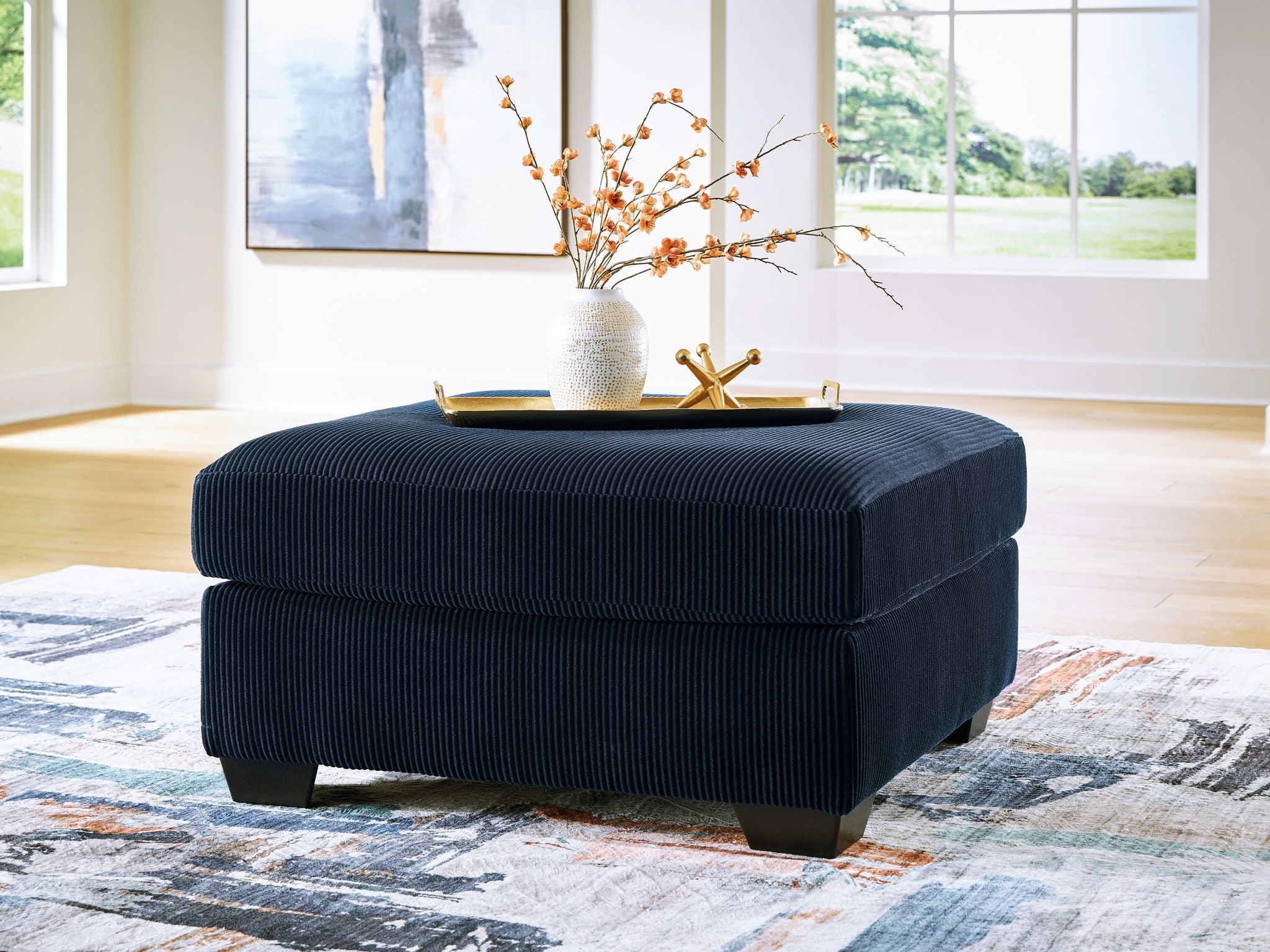 Navy oversized ottoman with ribbed fabric, square padded top, dark legs.