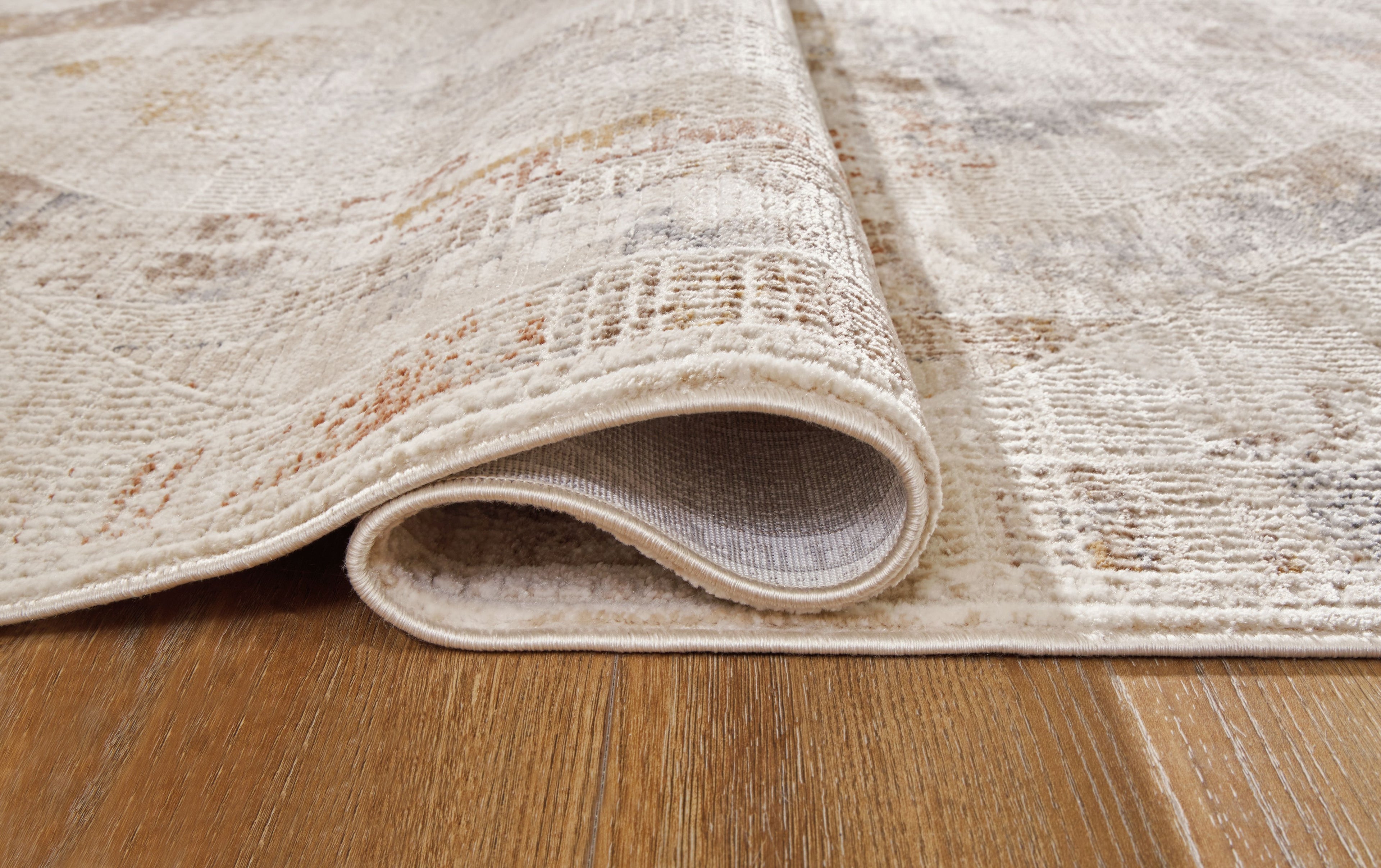 Beige and gray area rug with rolled edge showing low pile thickness.