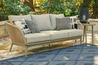 Beige wicker sofa with light gray cushions and patterned throw pillows