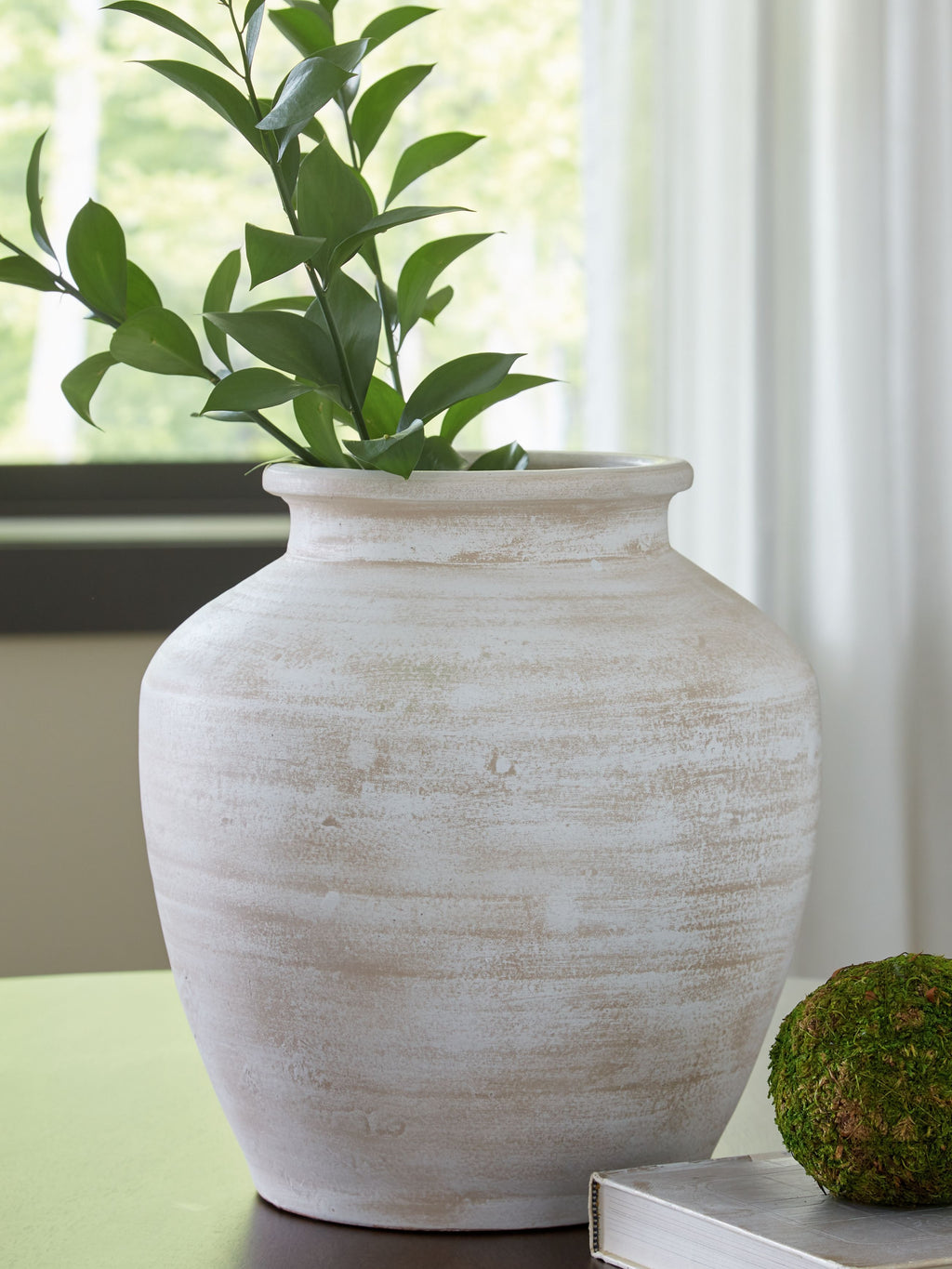 White ceramic vase with wide mouth holding leafy plant stems