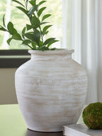 White ceramic vase with wide mouth holding leafy plant stems