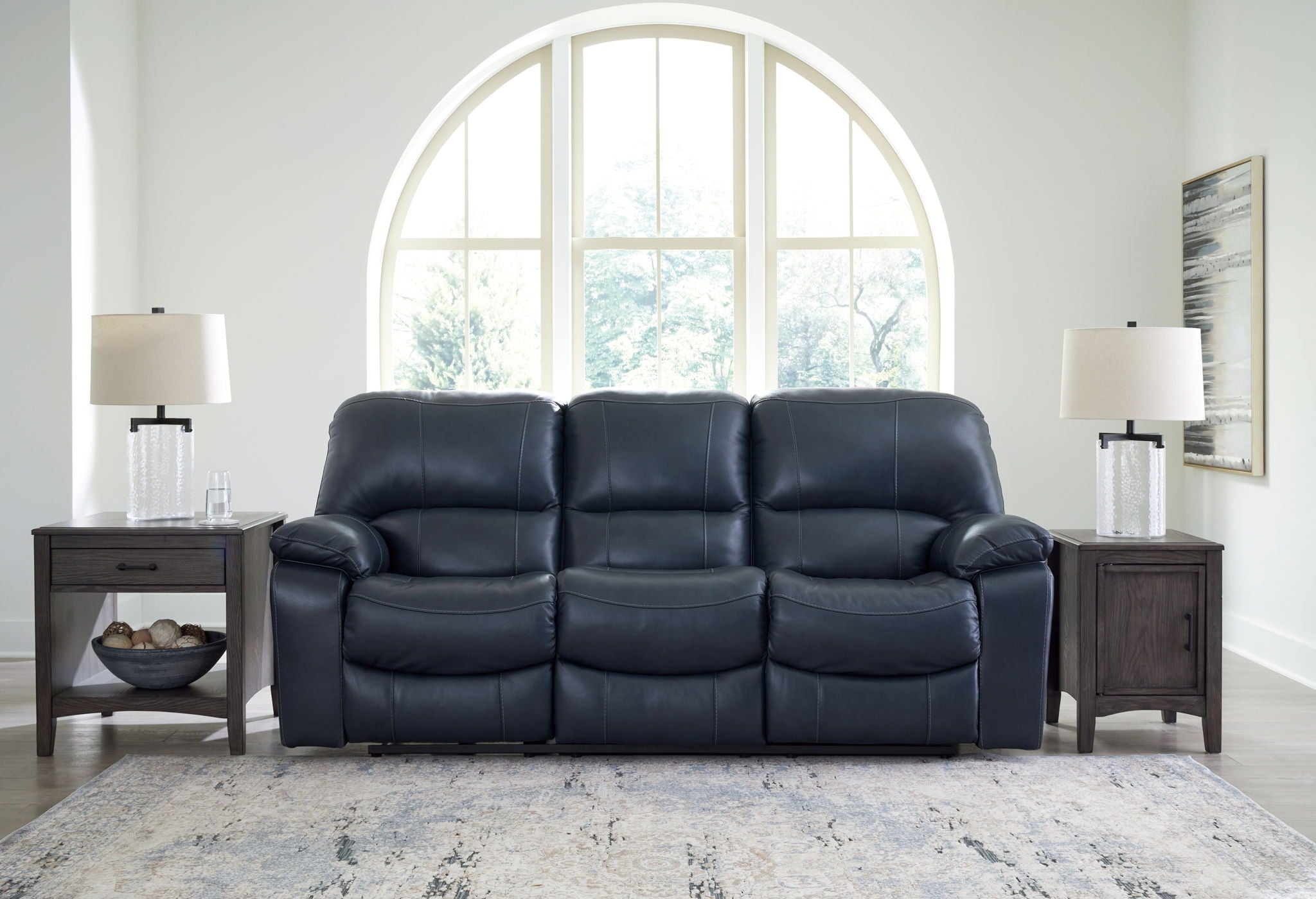 Power reclining sofa with dark navy leather-look upholstery and padded armrests