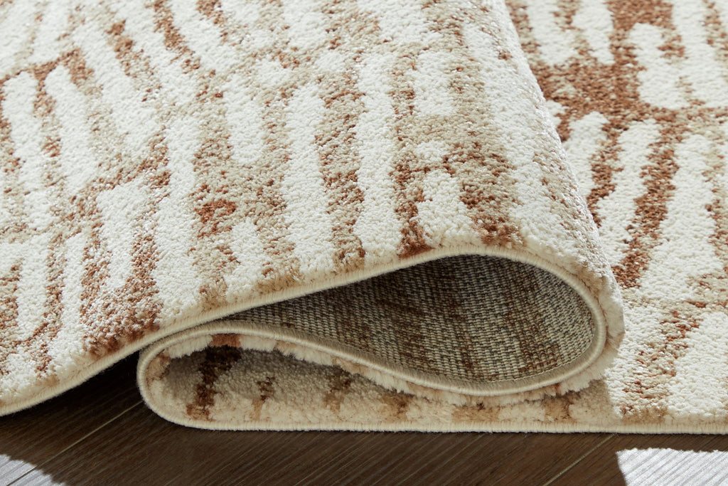 Area rug edge view: cream top with rust pattern and gray backing