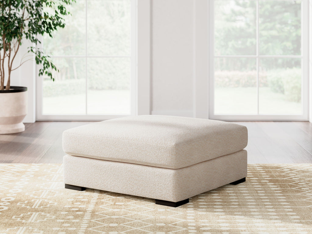 Vanilla upholstered ottoman centered in living room on patterned rug