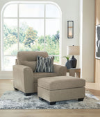 Light brown upholstered armchair with matching ottoman and striped throw pillows