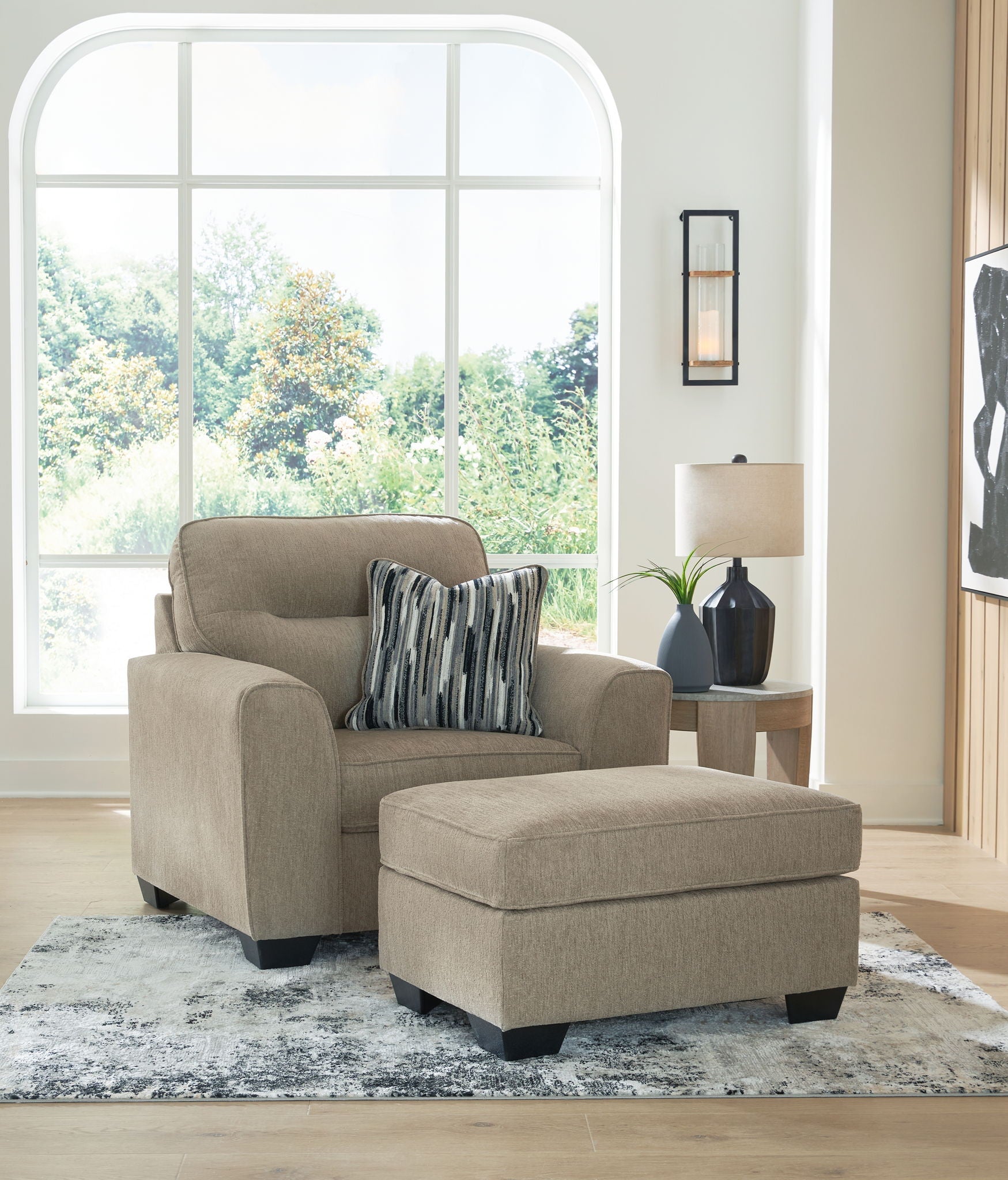 Light brown upholstered armchair with matching ottoman and striped throw pillows
