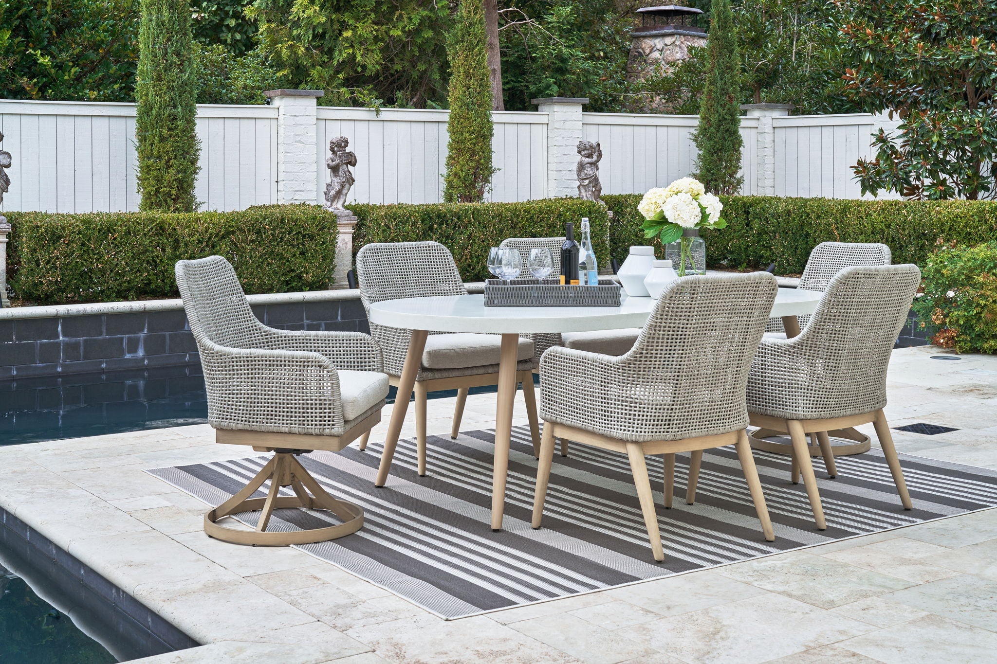 Outdoor dining set with multiple light gray arm chairs and table with glass top