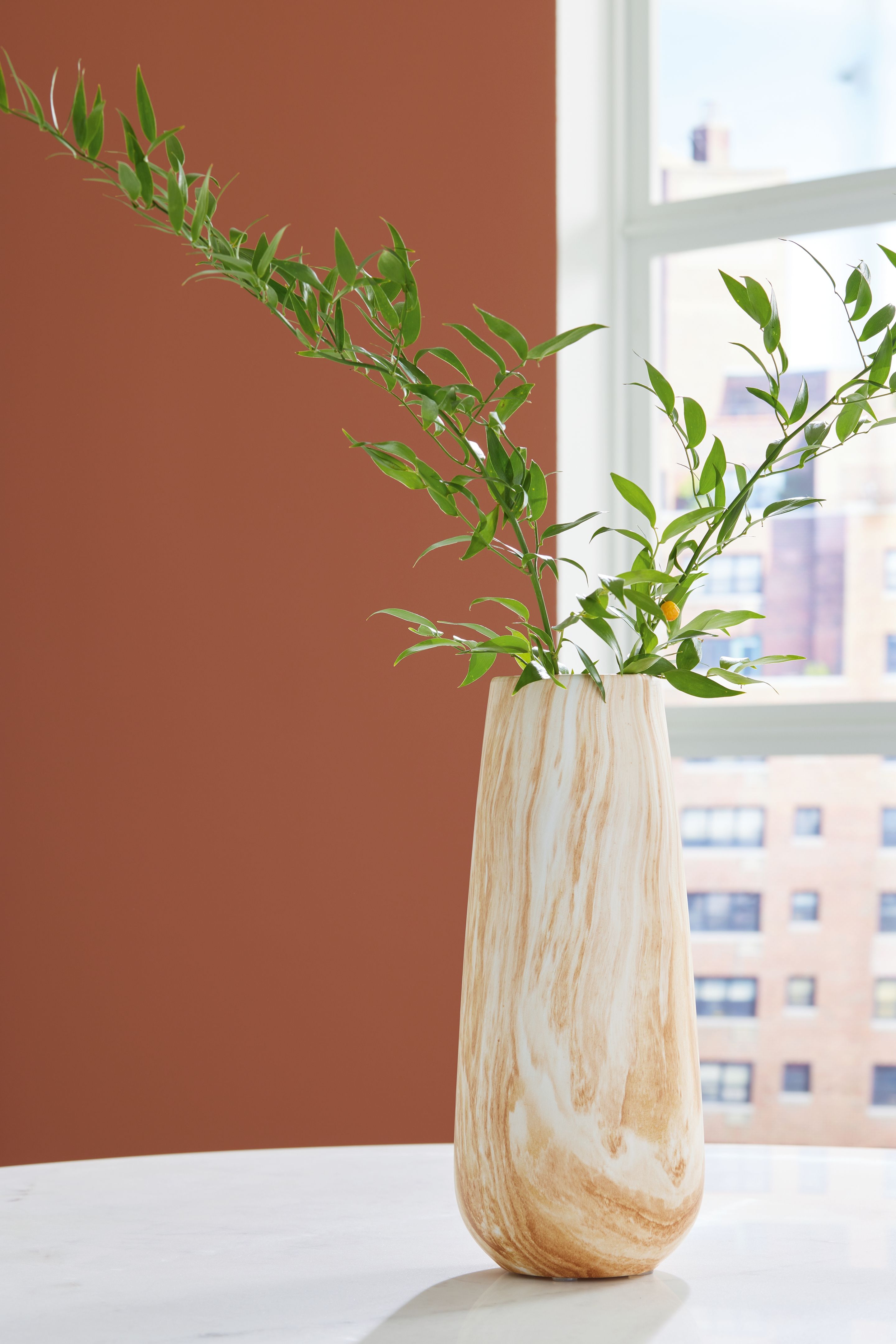 Beige marbled vase holding thin leafy stems, flared mouth and tall profile