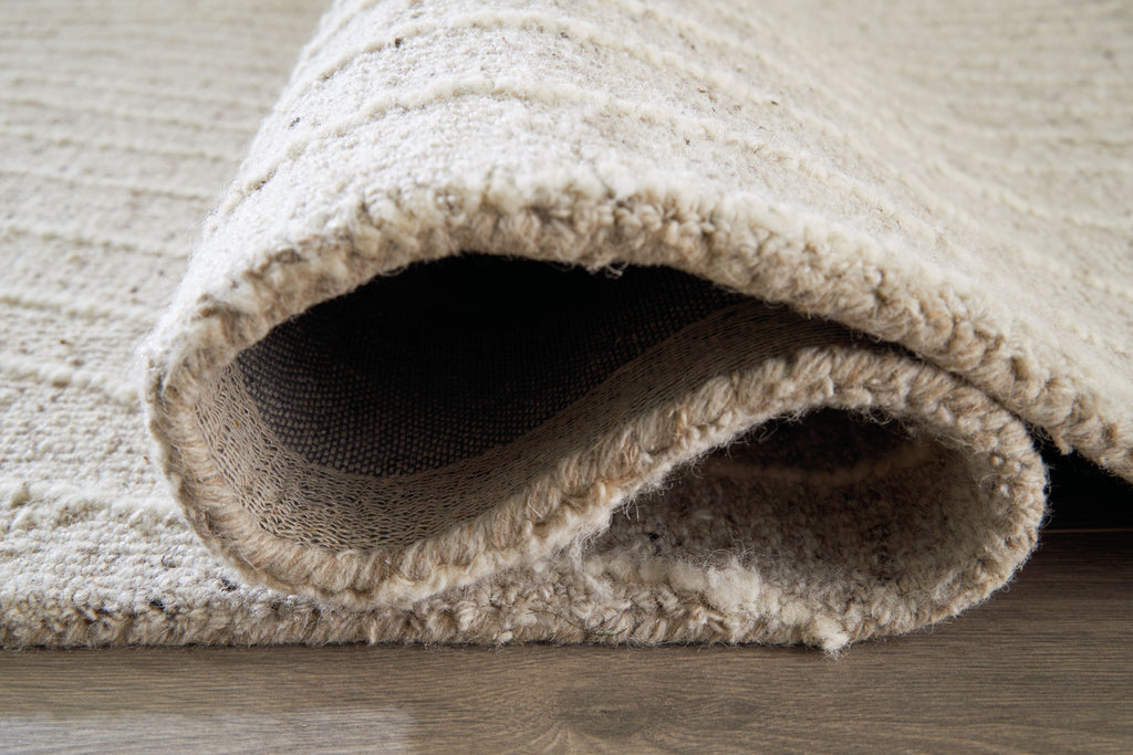 Cream rug showing folded edge with low pile and woven underside