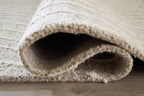 Cream rug showing folded edge with low pile and woven underside