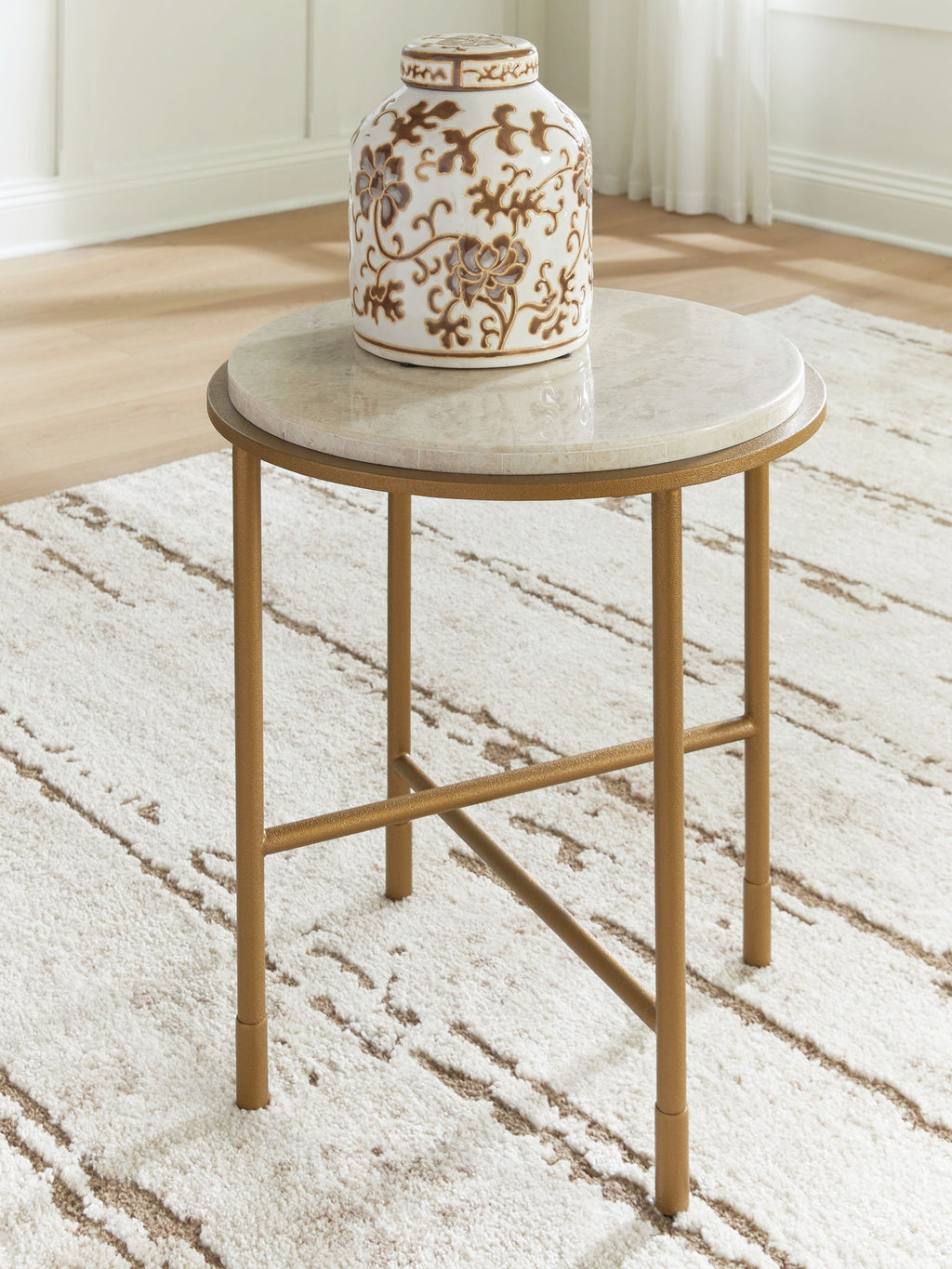 Round table with cream stone-look top and gold metal base, angled cross-brace view.