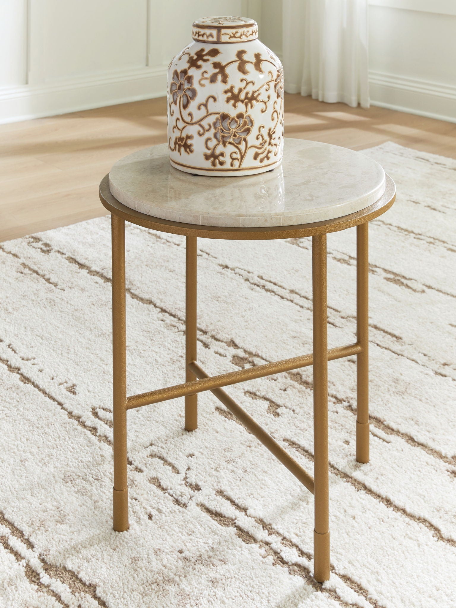 Round table with cream stone-look top and gold metal base, angled cross-brace view.