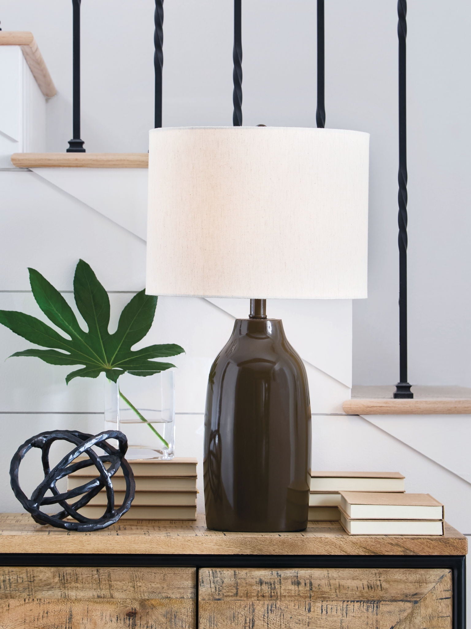 Brown bottle-style table lamp with white drum shade on a wooden console