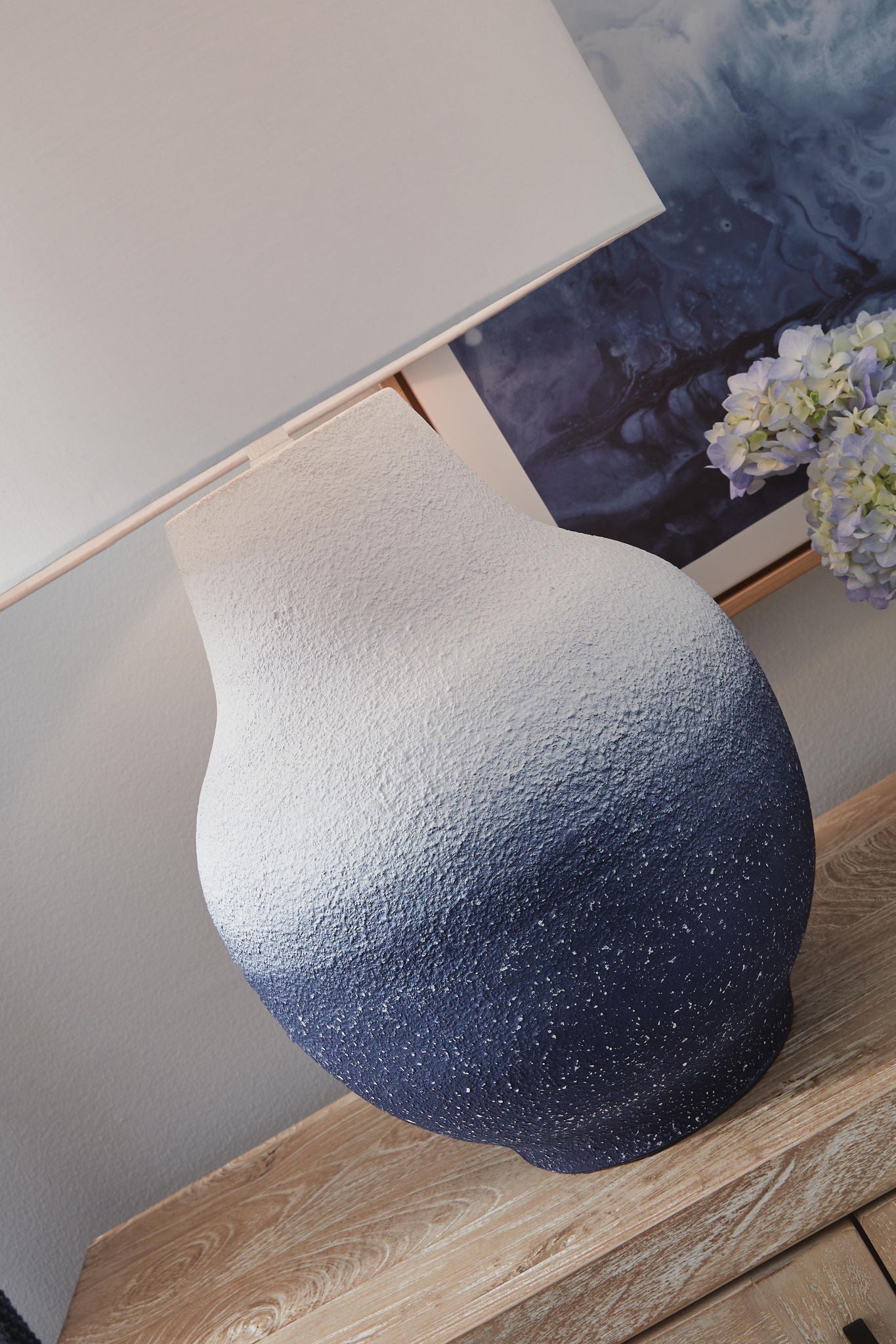 Metal table lamp with white drum shade and speckled navy base with textured finish