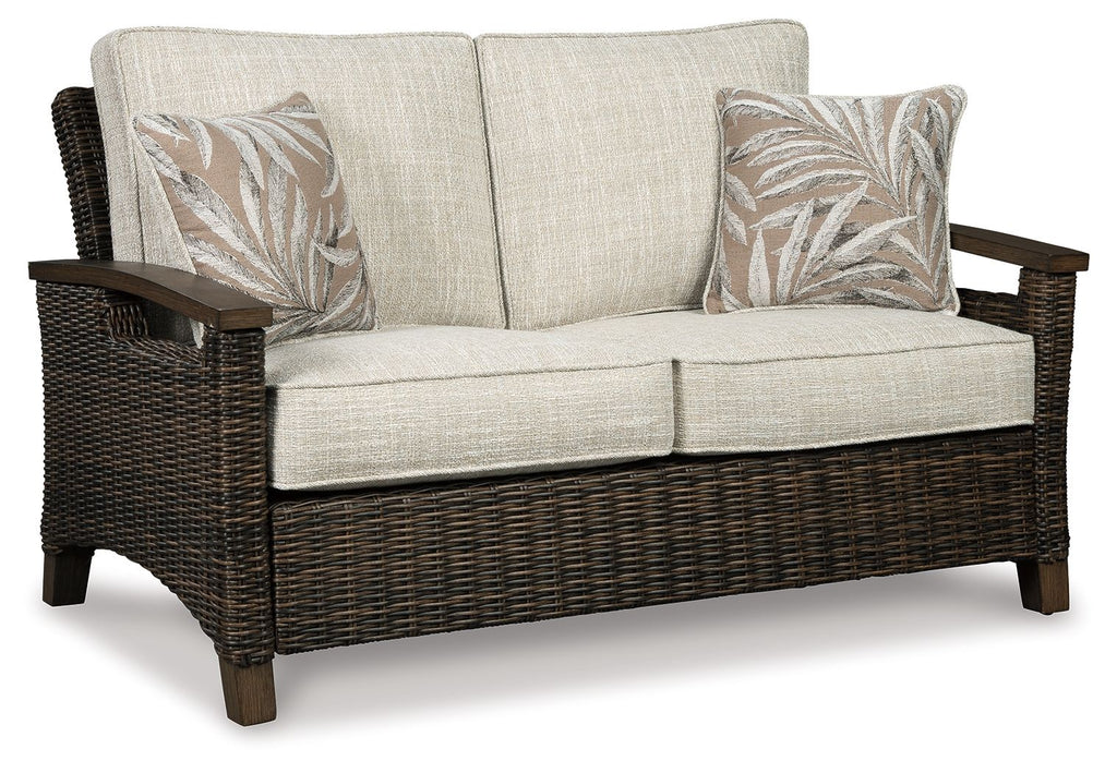 Loveseat with cushion, dark wicker arms, light beige seat and back, two leaf-print pillows