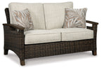 Loveseat with cushion, dark wicker arms, light beige seat and back, two leaf-print pillows