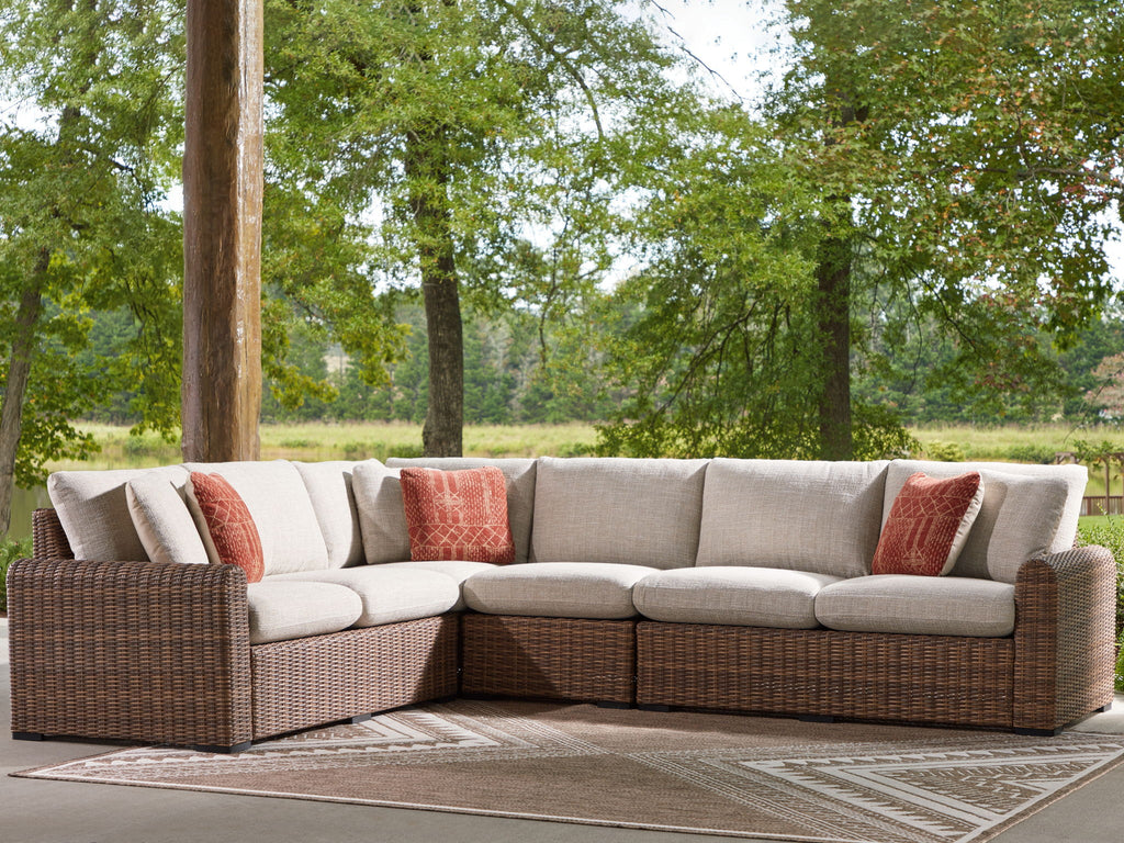 Outdoor sectional sofa with beige upholstery, brown wicker frame, and rust throw pillows