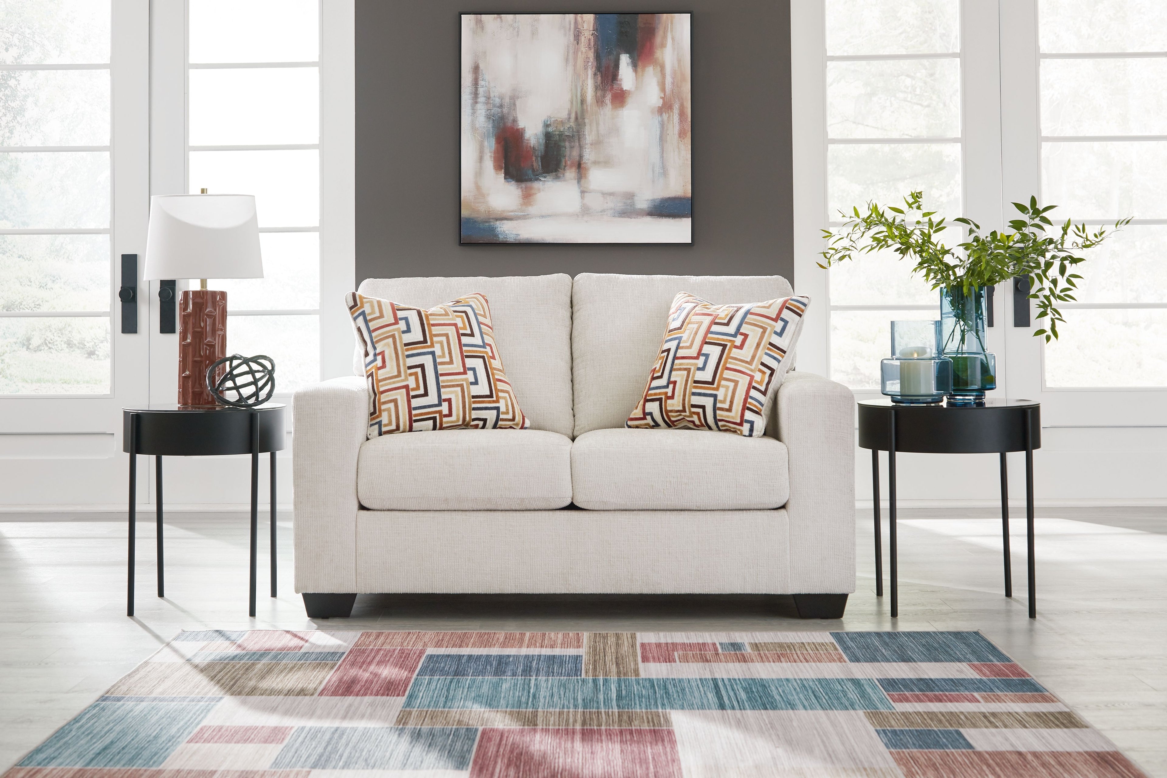 Light beige loveseat with two decorative geometric throw pillows and short legs.
