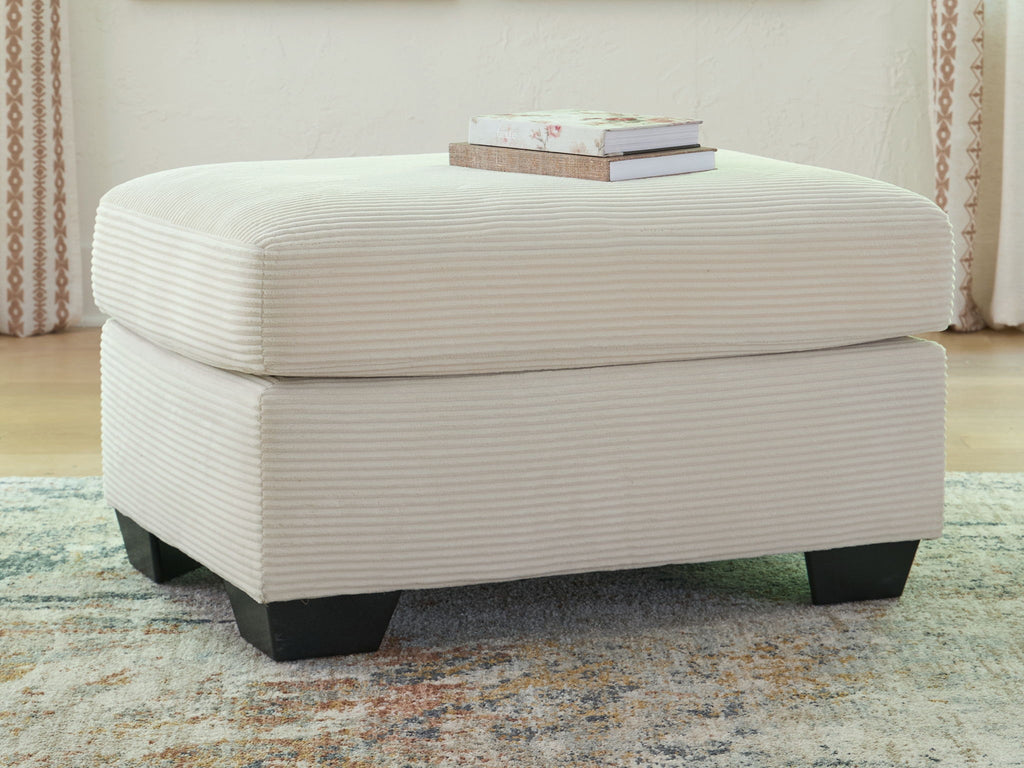 Cream upholstered ottoman with rounded lid, ribbed fabric texture, and dark legs