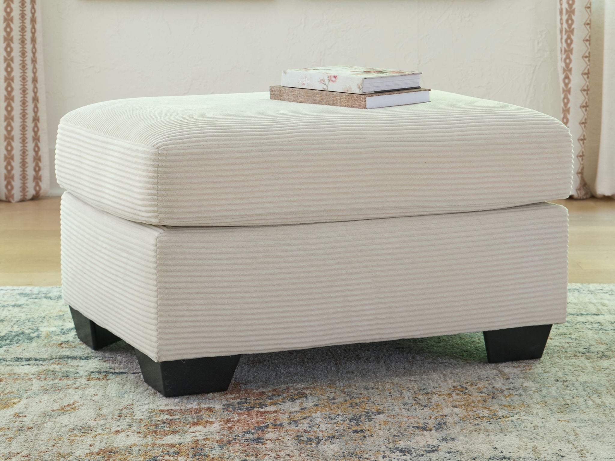 Cream upholstered ottoman with rounded lid, ribbed fabric texture, and dark legs