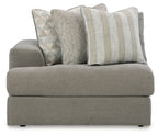 Gray upholstered corner chair with three patterned throw pillows and broad seat cushion