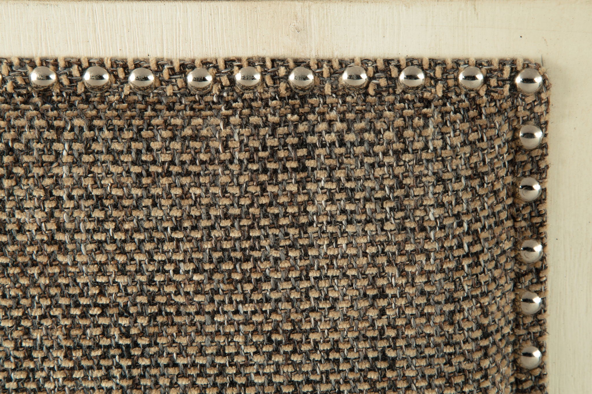Textured upholstered bench fabric corner with silver nailhead trim along edge