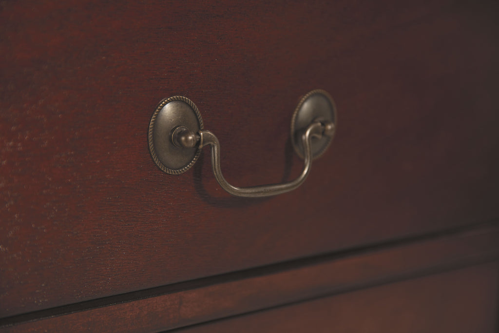 Nightstand drawer pull with curved metal U-handle on reddish brown wood