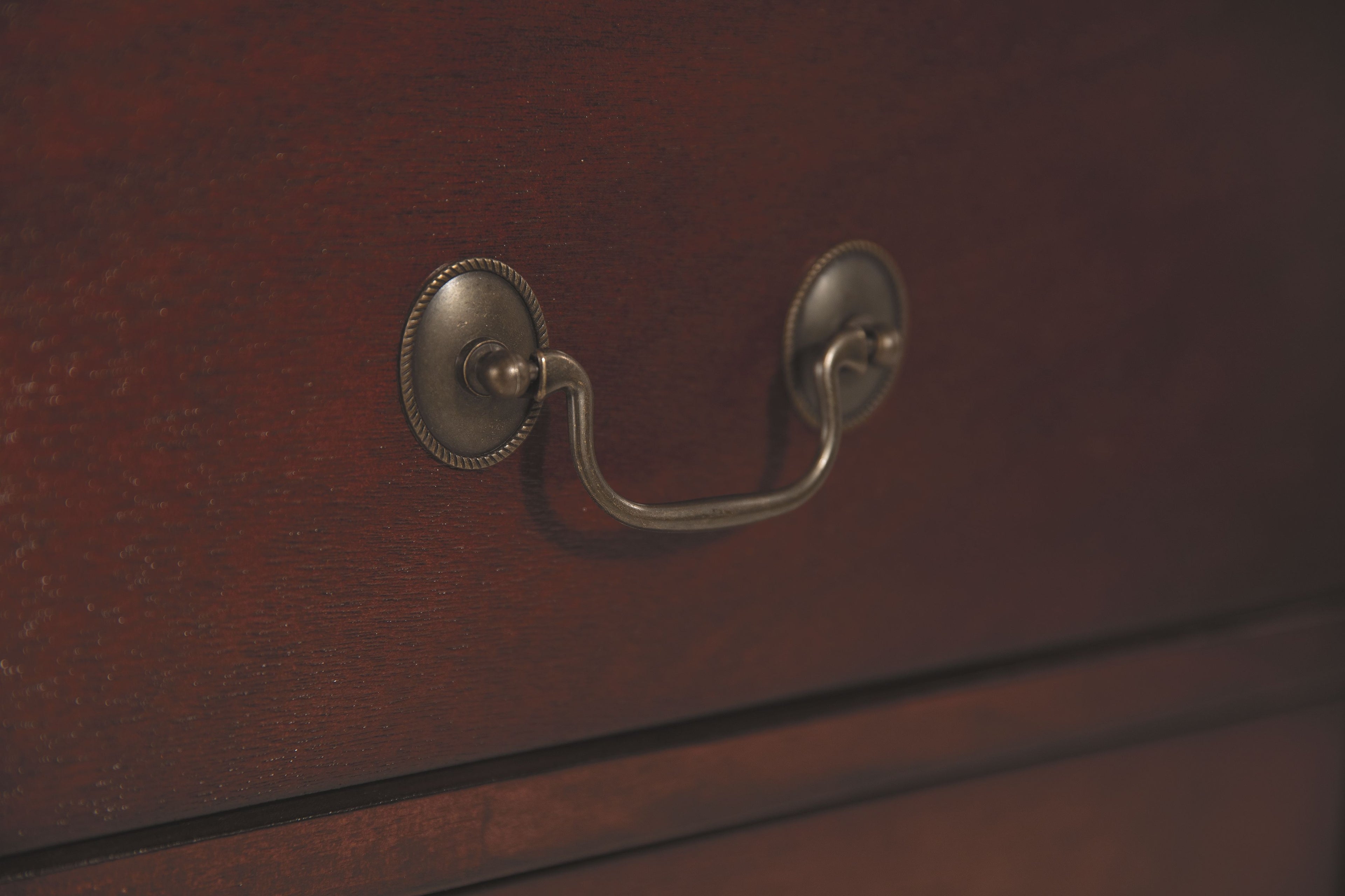 Nightstand drawer pull with curved metal U-handle on reddish brown wood