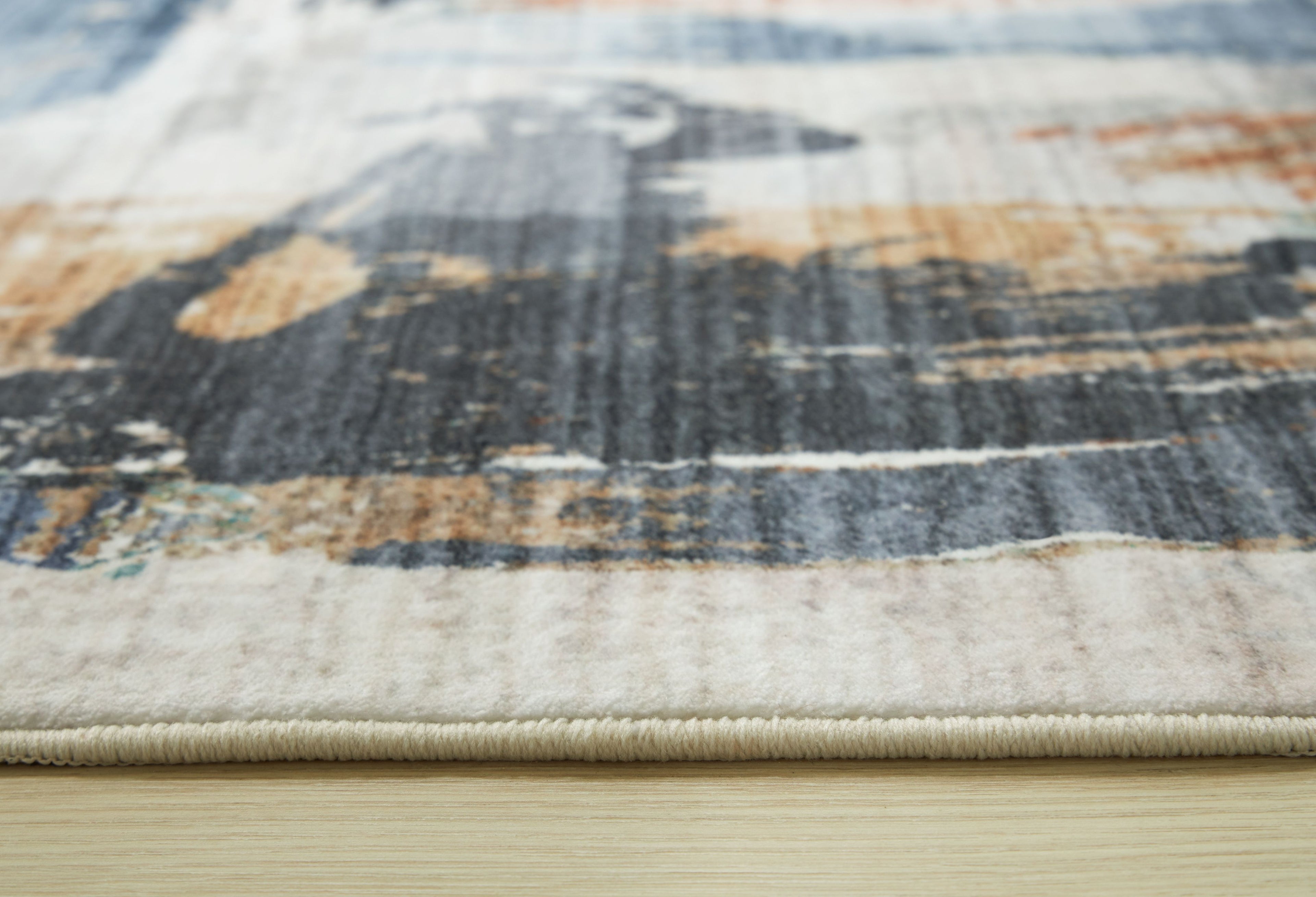 Washable rug close-up with abstract blue, beige, and rust pattern and flat edge