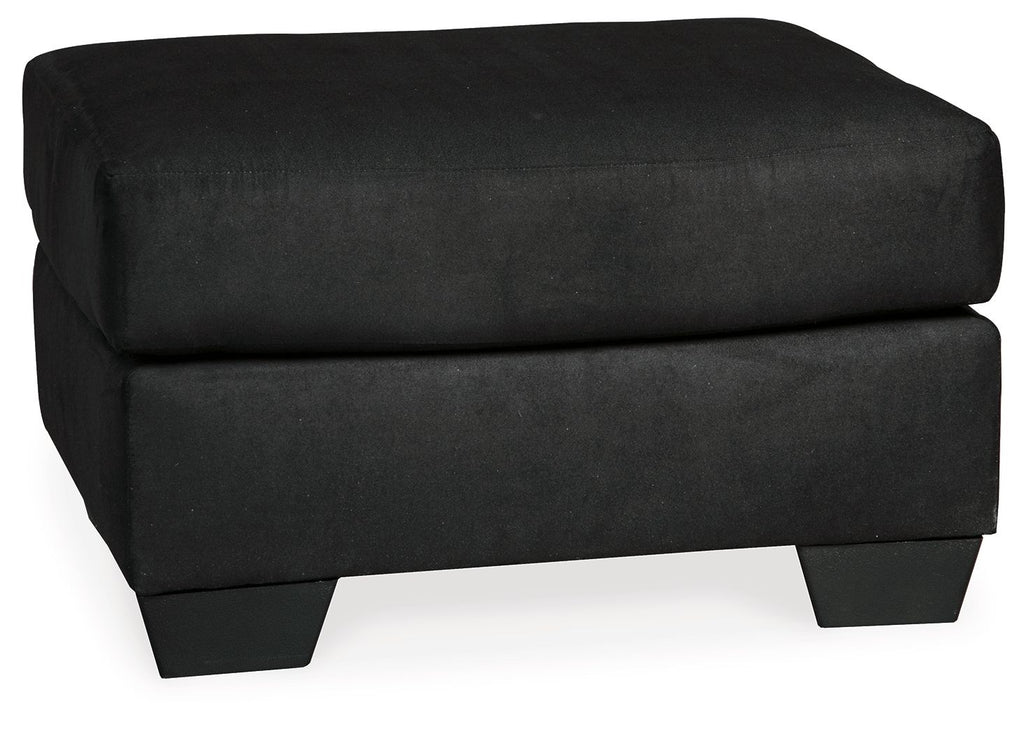 Black upholstered ottoman with rounded top cushion and short dark legs.