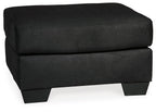 Black upholstered ottoman with rounded top cushion and short dark legs.