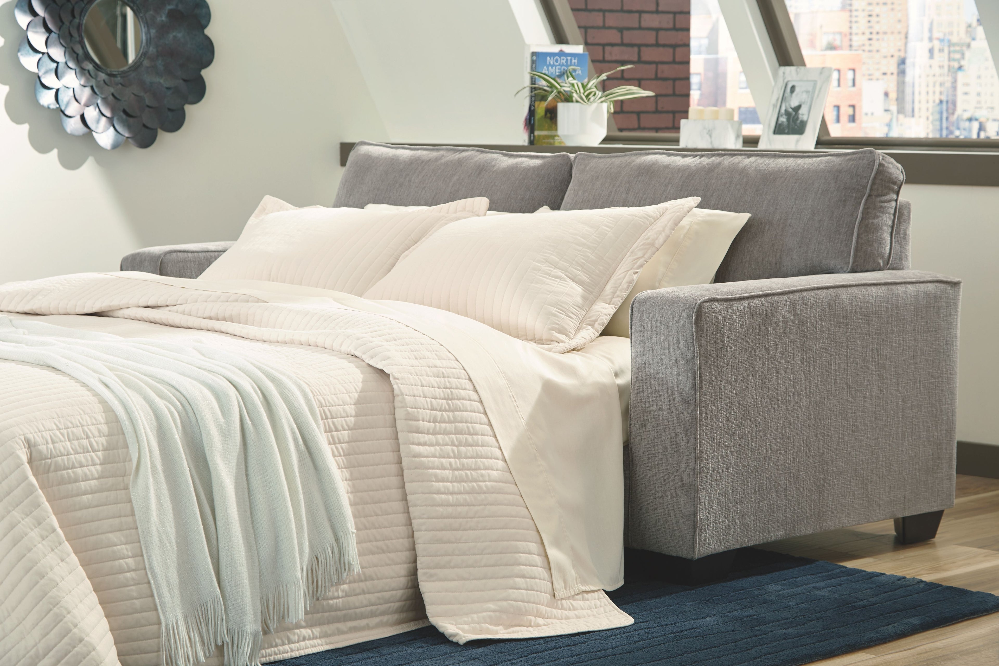 Slate sleeper sofa with extended mattress and white bedding and pillows