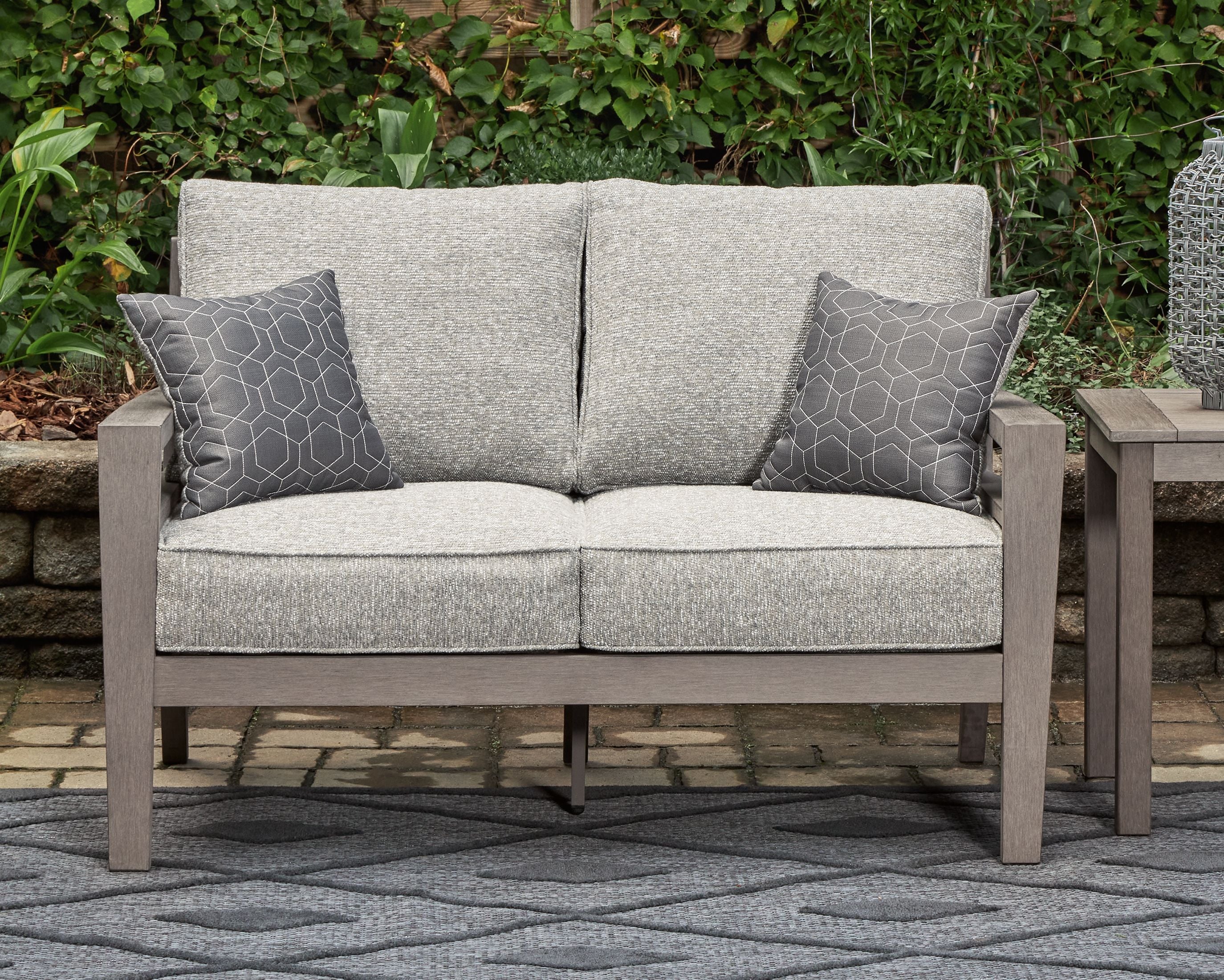 Gray loveseat with two square patterned throw pillows and twin seat cushions