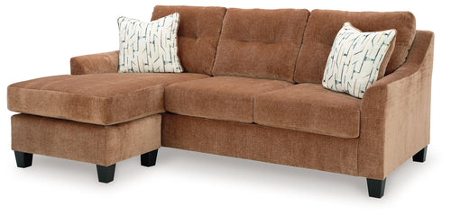Clay sofa chaise in L-shape with two patterned pillows and padded armrests