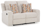 Reclining loveseat with light beige upholstery and two patterned throw pillows