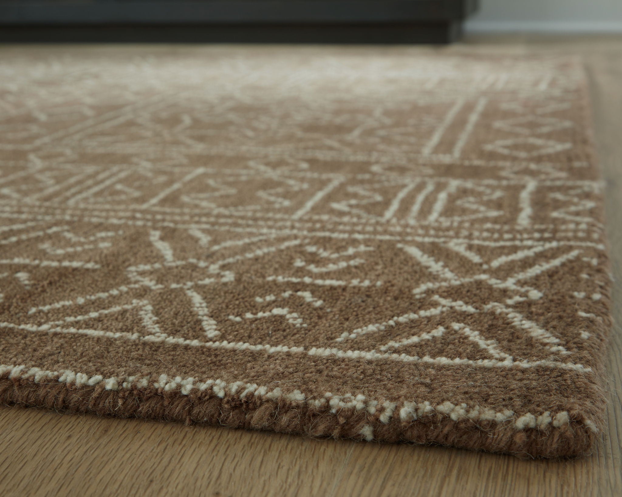 Textured rug close-up with dark brown pattern lines on beige background and trim
