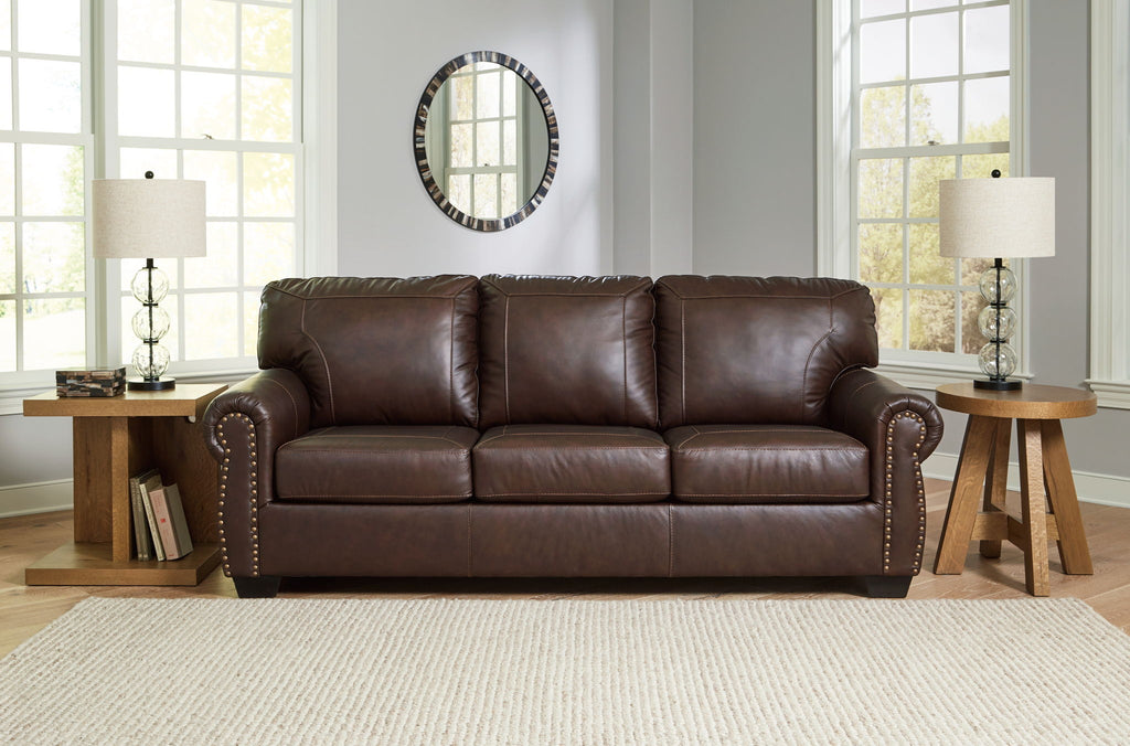 Dark brown upholstered sofa with tufted back cushions and nailhead trim