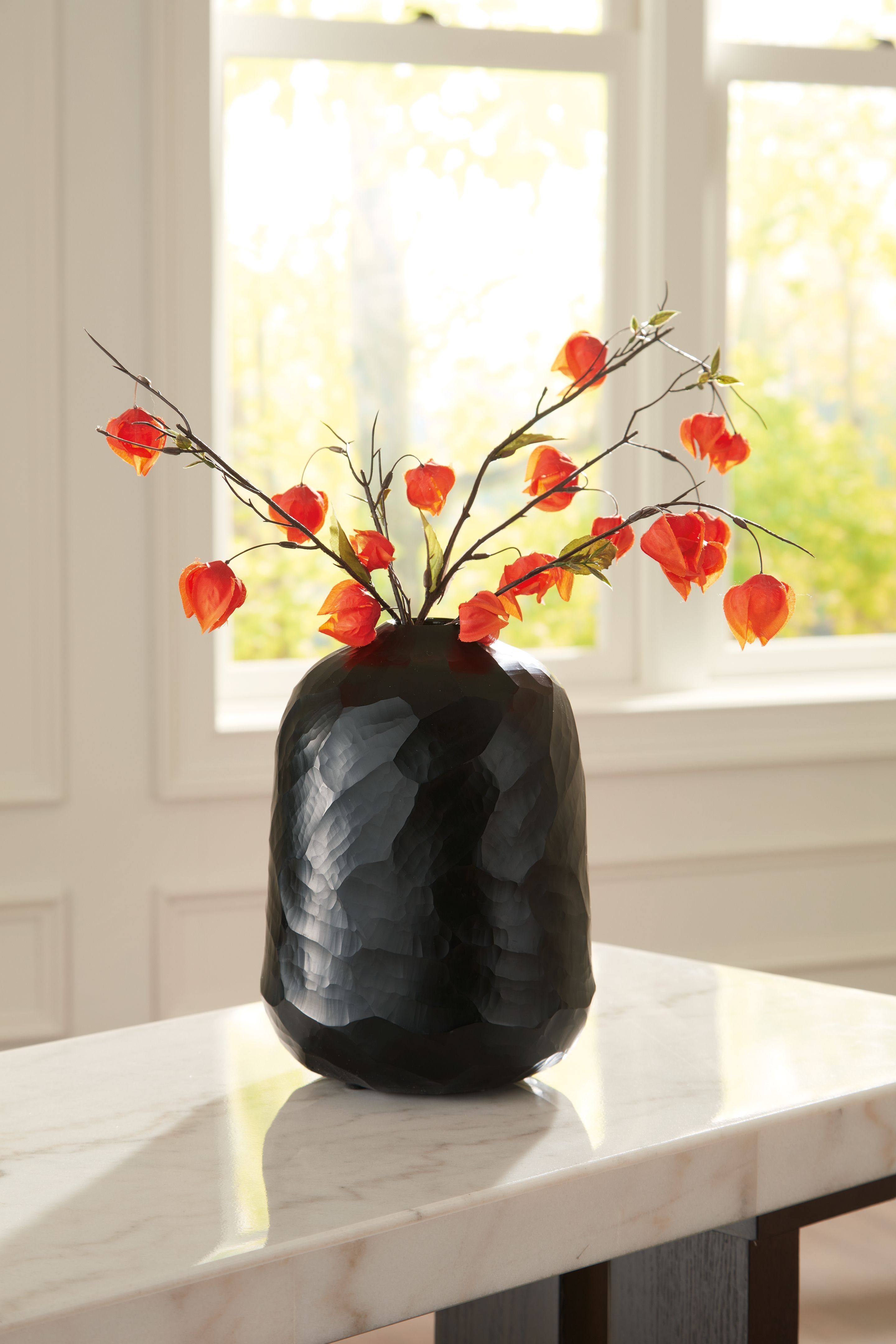 Black faceted vase with red flowers on tabletop surface