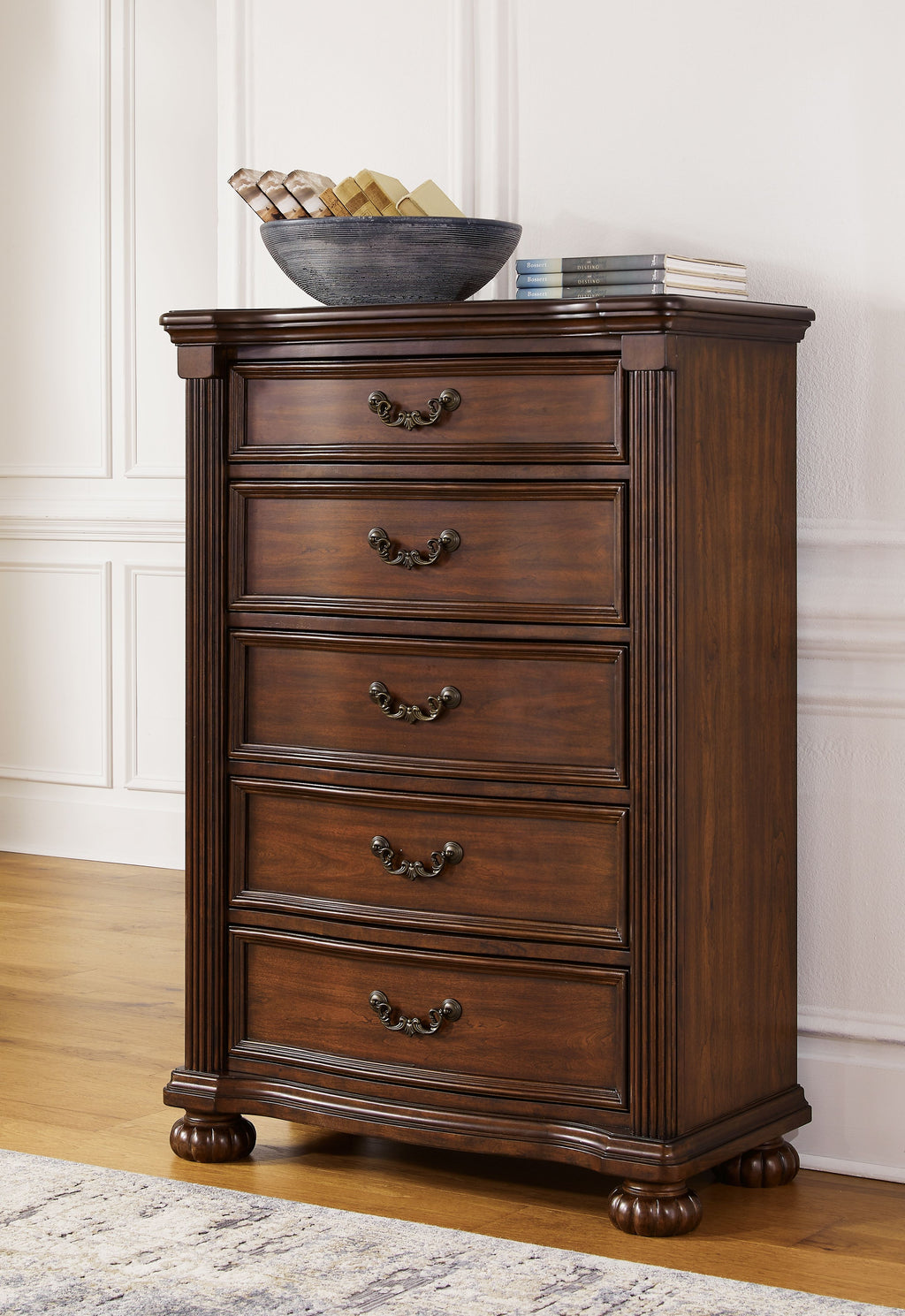 Brown five-drawer chest with decorative metal pulls and carved wood base