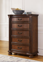 Brown five-drawer chest with decorative metal pulls and carved wood base